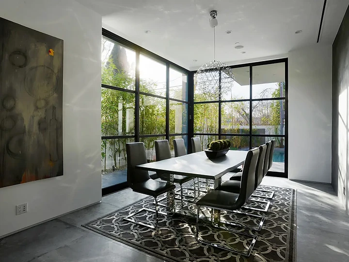 A white dining table and black chairs beside a large dark canvas and steel-framed glass, an interior by Apel Design
