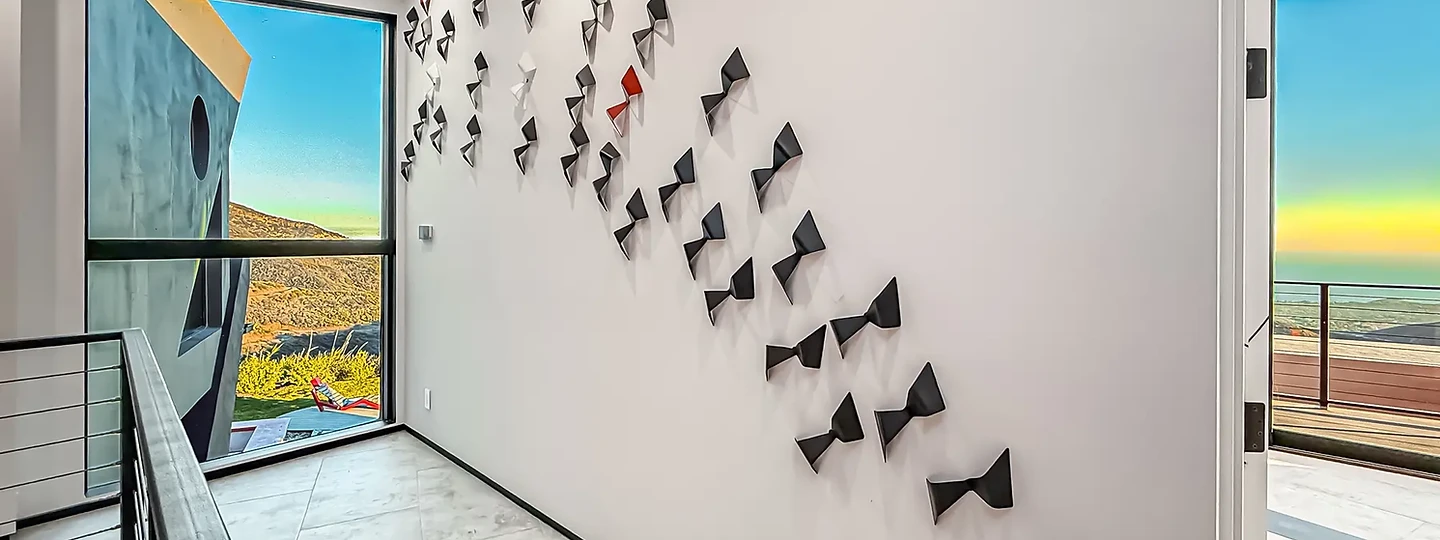 Black and red sculptures on a white wall beside a tall window, at The Aviator in Malibu, by Apel Design