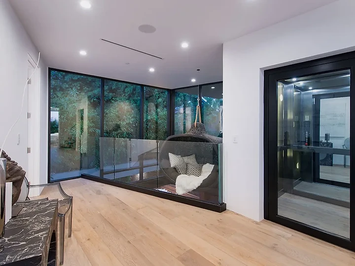A tall black-framed glass door and a corner of floor-to-ceiling glass facing a garden, an interior by Apel Design