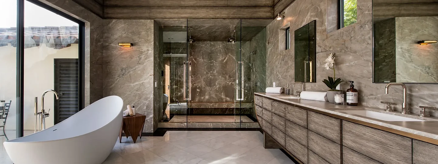 Gray stone walls and a long grained wood vanity beside a sculptural tub, an interior by Apel Design