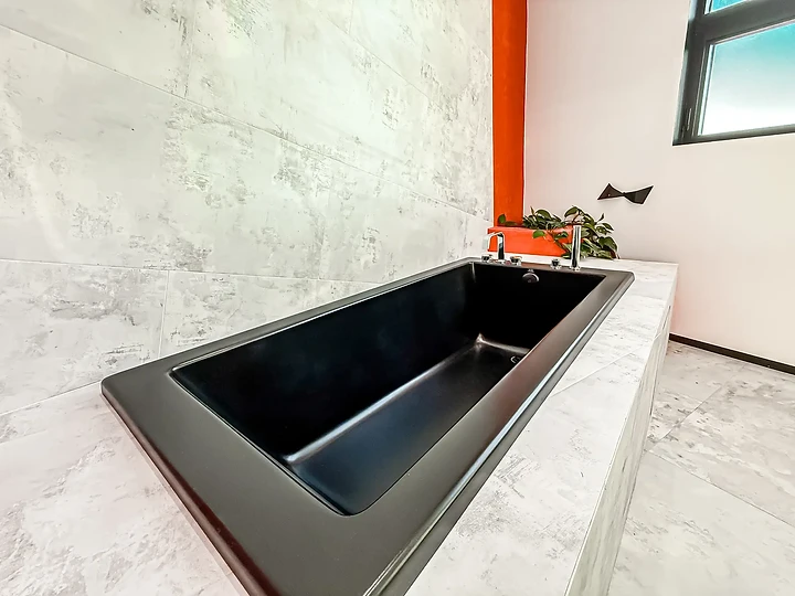 Black tub set in a pale veined deck below an orange wall, at The Aviator in Malibu, by Apel Design