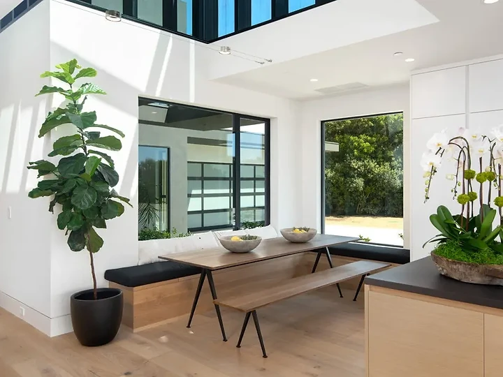 A wood dining table and benches beside tall garden windows, with high glazing above, an interior by Apel Design