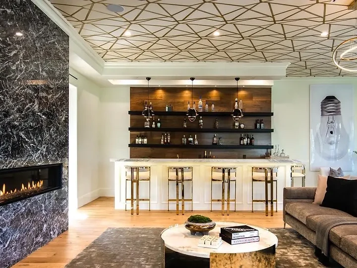 A lounge bar with dark wood shelves and gold-toned stools beside a black stone fireplace, an interior by Apel Design