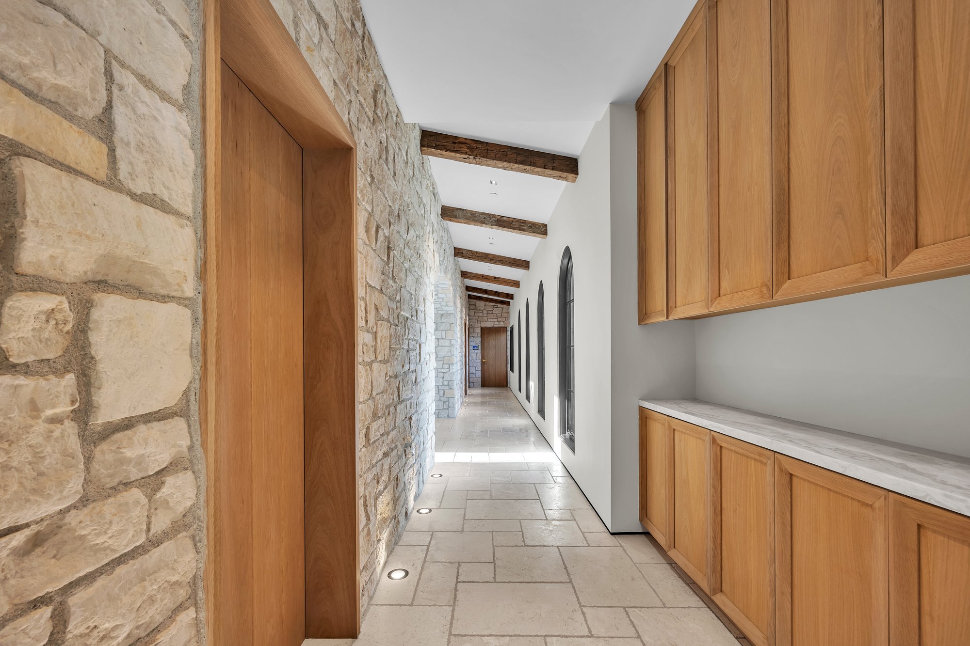 A stone-walled hall lined with timber cabinetry, Merritt Estate in Malibu by Apel Design
