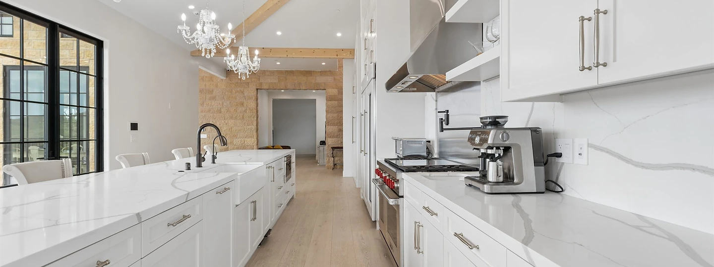 Long white kitchen at Oya with a vaulted ceiling, chandeliers and marble counters