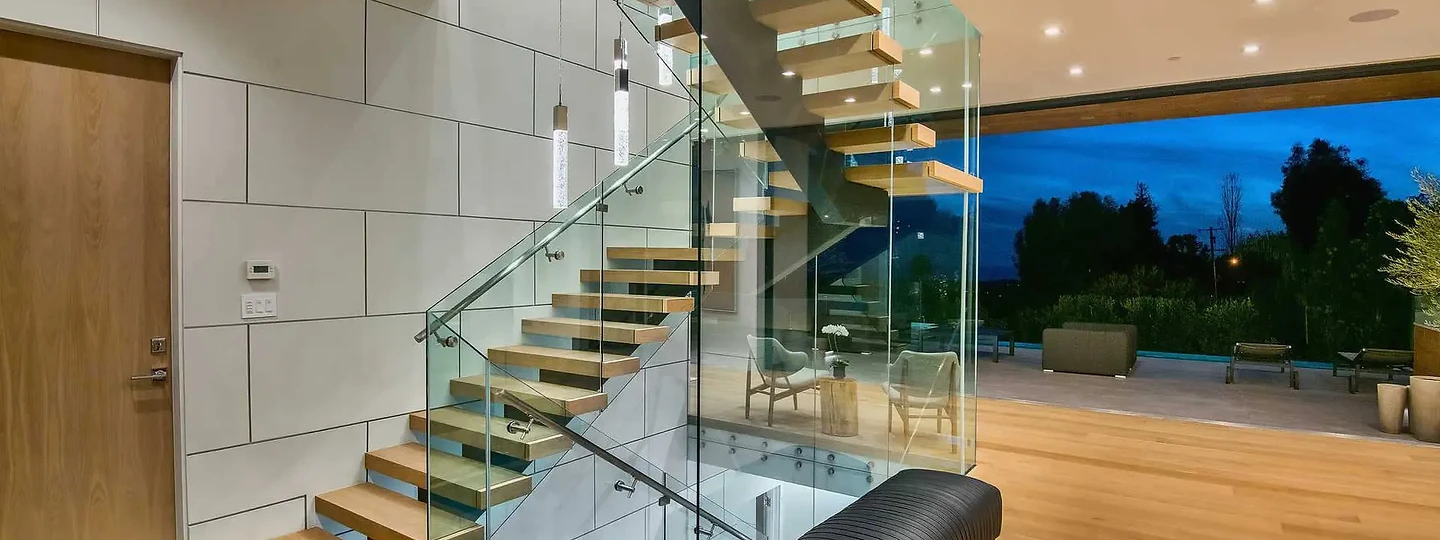 Timber treads on a steel spine rise inside a glass stairwell beside the entry, an interior by Apel Design