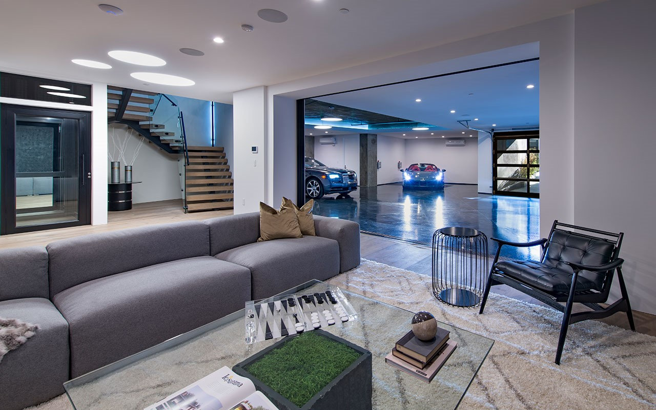 Lower-level lounge at Shoreham with open-riser stair, glass elevator and garage beyond, by Apel Design