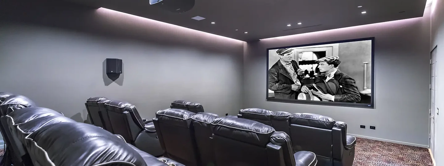 A grey theater with two tiers of black reclining seats and soft cove lighting, an interior by Apel Design