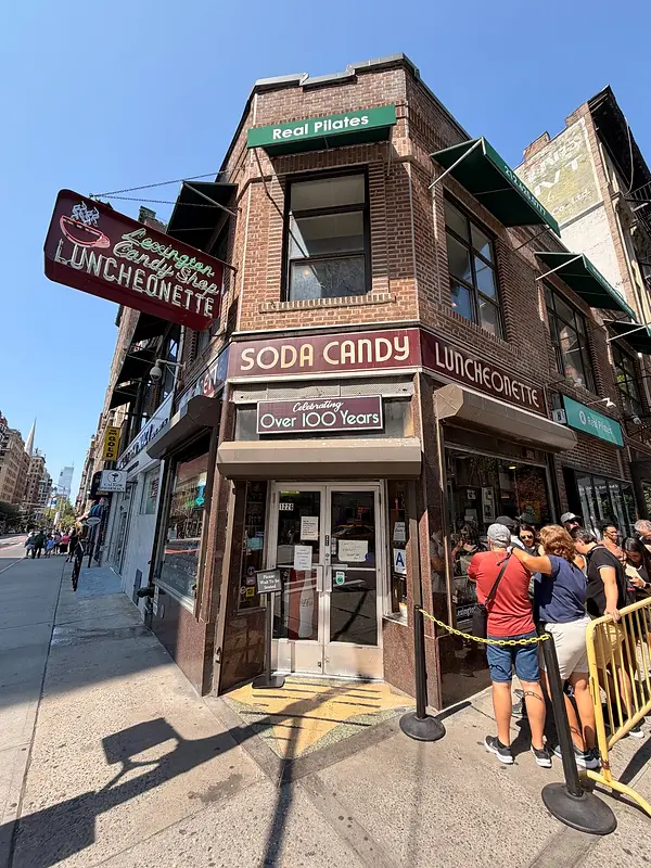 Corner exterior of Lexington Candy Shop on the Upper East Side, with vintage soda-candy-luncheonette signs and customers gathering beside the entrance.
