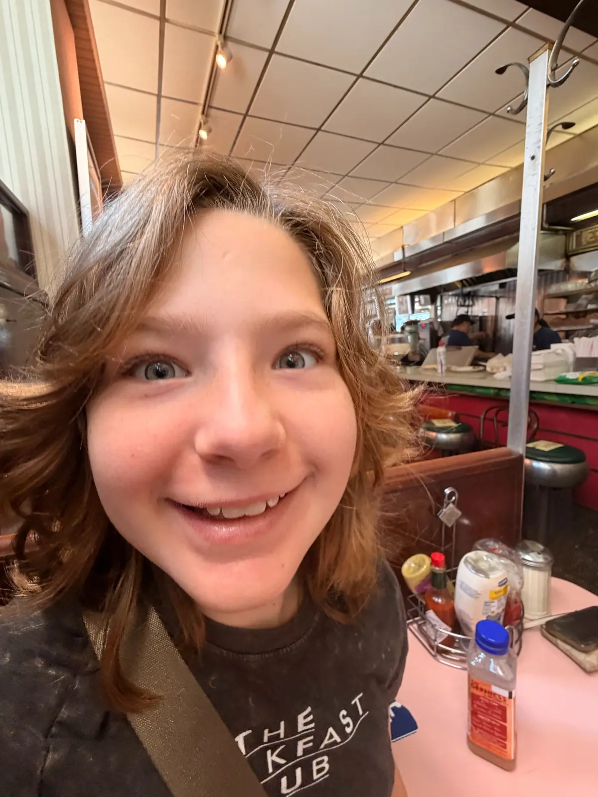 Close selfie of Olivia inside Lexington Candy Shop with the counter, stools, and tabletop condiments visible behind her.