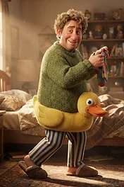 A friendly man with curly brown hair wearing a green sweater and a yellow duck floatie around his waist, standing in a cozy bedroom while holding a colorful sock.