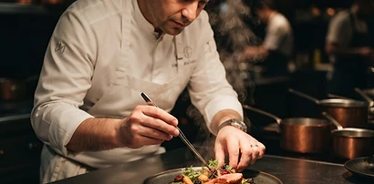 A chef in a white uniform plating a gourmet dish in a modern kitchen