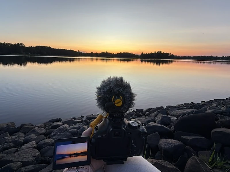A filmmaker's camera on a rocky shoreline capturing a sunset over a Wisconsin lake