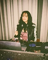 Mia Nirvana behind the booth, eyes closed in a warm smile, headphones around her neck
