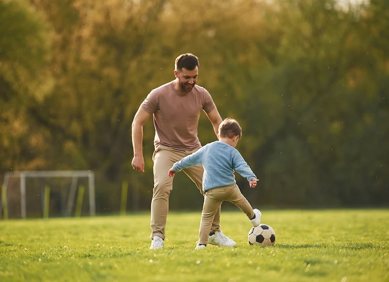 A father and son playing soccer at golden hour