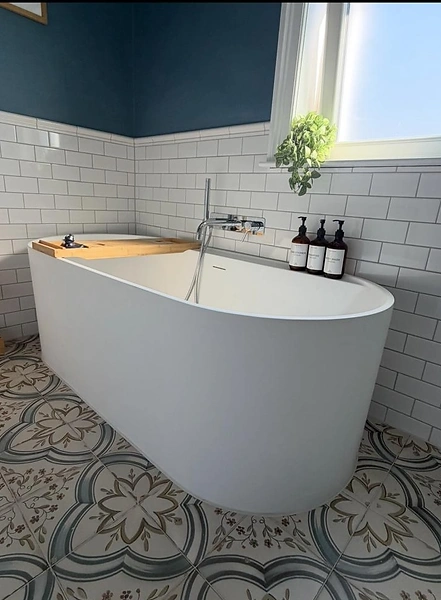 Freestanding oval bathtub against a deep blue tiled feature wall