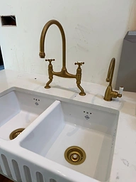 White farmhouse kitchen sink with brass cross-handle faucets