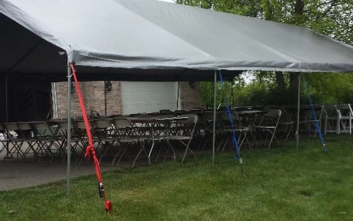 Frame tent with chairs and tables set up on pavement and lawn