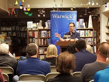 G. Brian Benson speaking in front of bookshelves