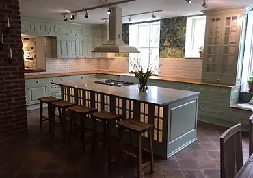 Platsbyggt kök med salviagröna luckor, köksö, träbänkskiva och terracottagolv