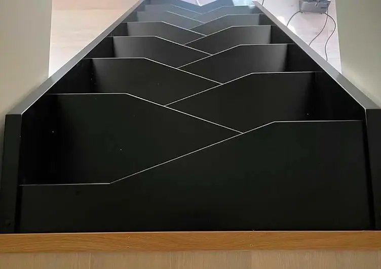 Trappa sedd uppifrån med svart geometriskt räcke och eksteg
