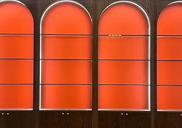 Mörk displayvägg med välvda glashyllor, orange bakpaneler och integrerad LED-belysning