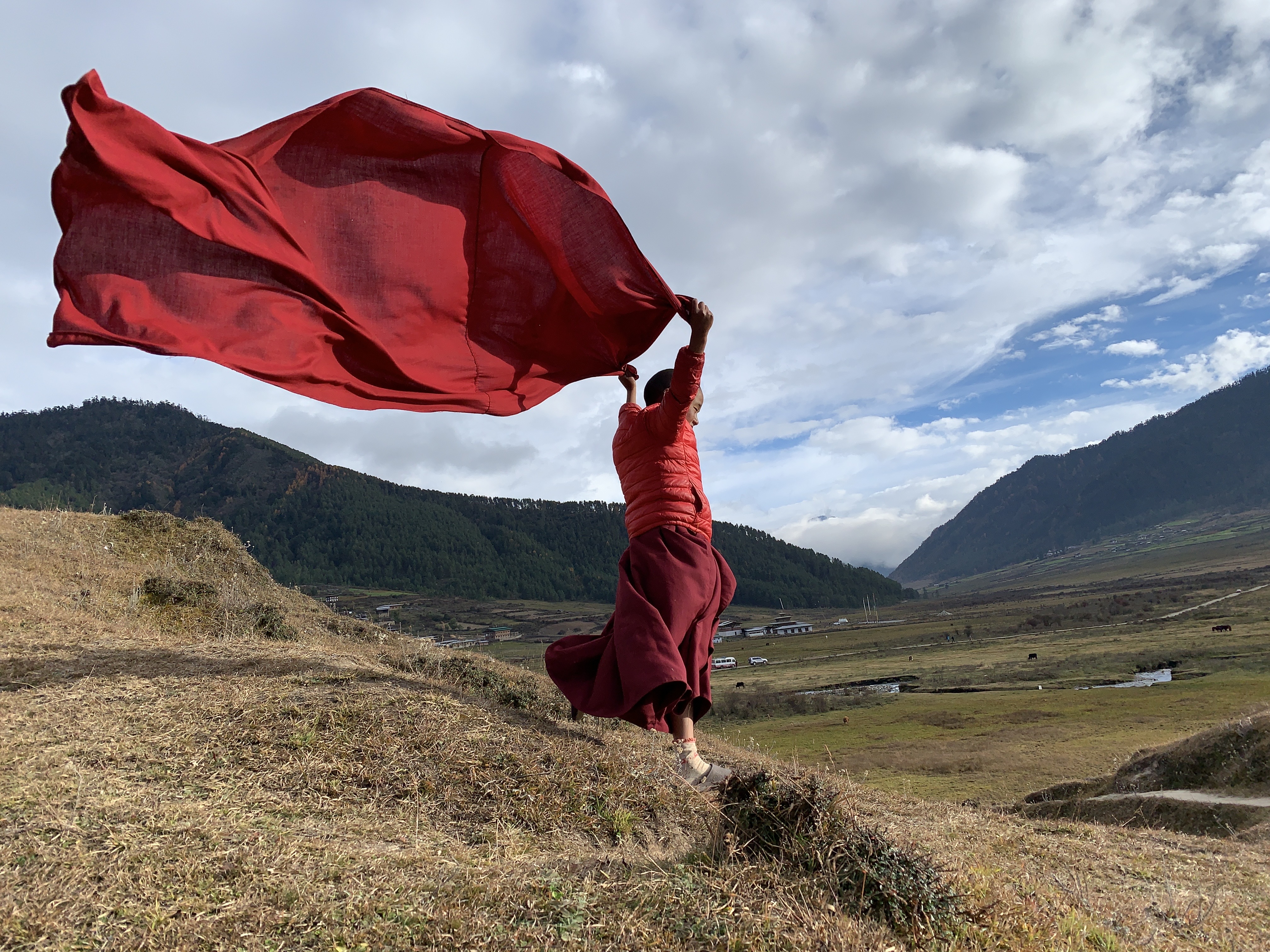 A monk holding red fabric aloft in a Himalayan valley
