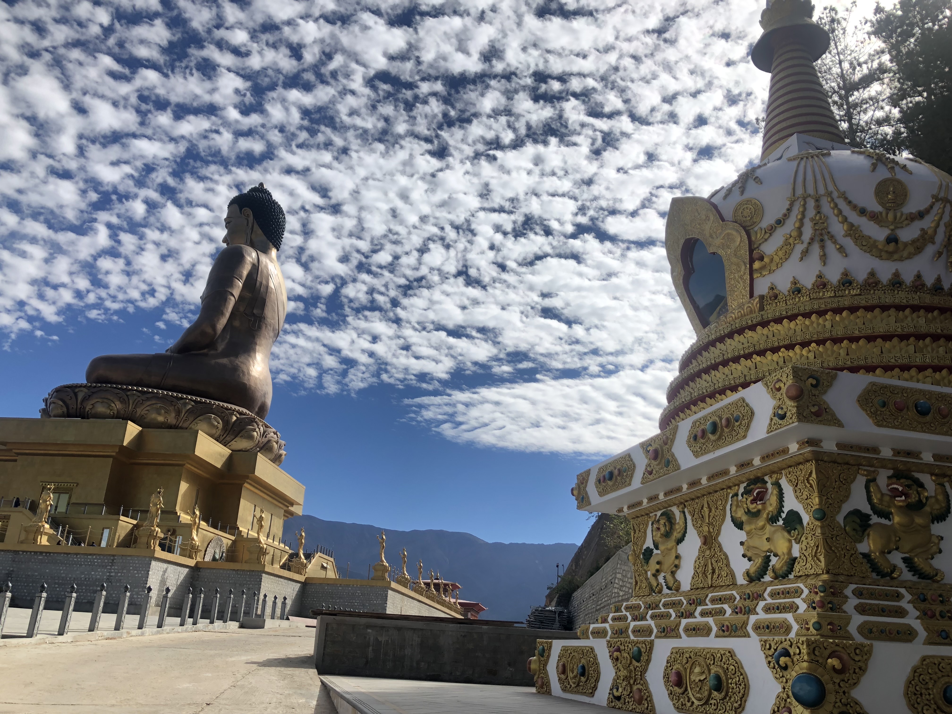 A golden Buddha statue and ornate stupa beneath a blue sky