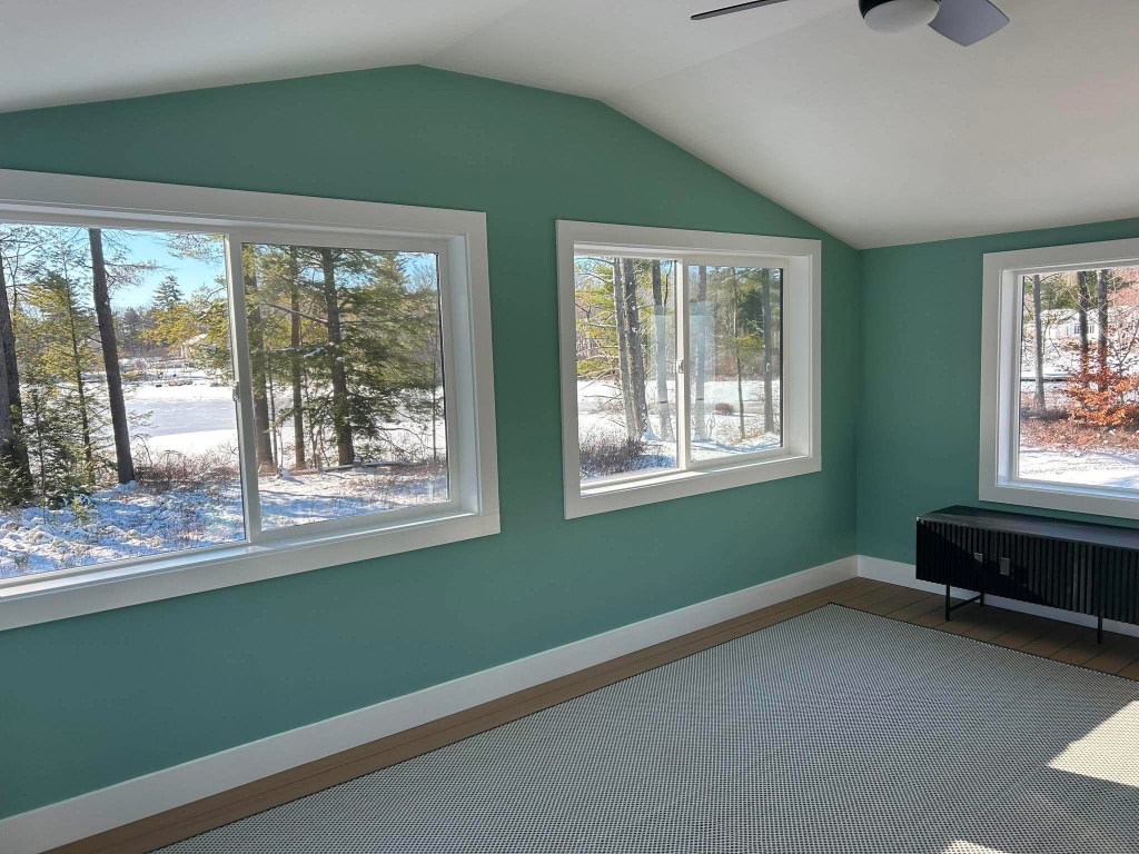 Bright vaulted living room with soft sage green walls, crisp white trim, and snowy woodland views painted by Boccio Painting LLC