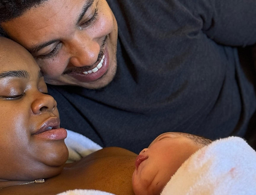 Black mother holding her newborn skin-to-skin as her partner embraces them moments after birth