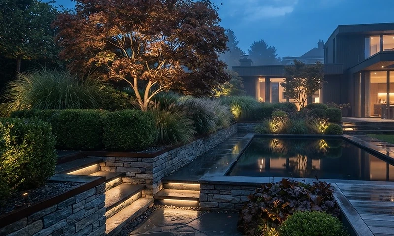 Designed garden terrace at dusk with uplit specimen planting and still water