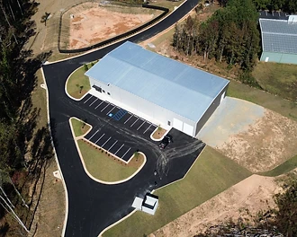 Aerial view of GTD Loop Industrial Building showing the metal-roofed facility, paved parking lot with striped spaces, and the cleared, forested site at GTD Loop