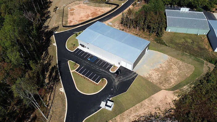 Aerial view of GTD Loop Industrial Building showing the metal-roofed facility, paved parking lot with striped spaces, and the cleared, forested site at GTD Loop