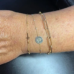 Three stacked gold permanent bracelets with cross charm and engraved floral charm by Oh She Linked