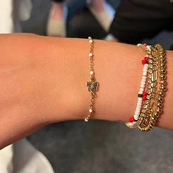 Gold permanent chain with white beads and blue butterfly charm paired with stacked beaded bracelets by Oh She Linked