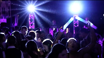 High school students dancing at a prom with glowing LED foam sticks under blue and purple stage lighting