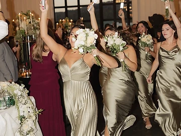 Bridesmaids in olive green gowns carrying glowing light tubes as they enter the reception hall at The Lookout at Greek Peak Mountain Resort