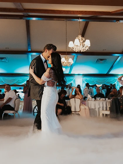 Bride and groom in a dip during their first dance surrounded by low fog and blue uplighting in a banquet hall