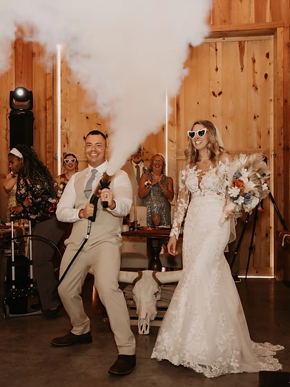 Groom firing a CO₂ confetti cannon beside his smiling bride wearing heart sunglasses at their wedding reception
