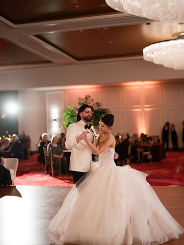 Bride and groom dancing in the Oneida Room at Turning Stone, the bride's white gown flared mid-movement, with warm uplighting and crystal chandeliers overhead
