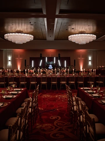 The Oneida Room at Turning Stone set for a wedding reception with crimson tablecloths, crystal chandeliers and a glowing AP monogram on the DJ stage