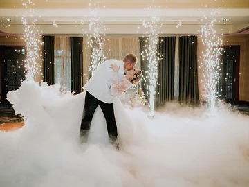 Bride and groom sharing a dip kiss surrounded by dancing-on-a-cloud fog and sparkler fountains at their Shenandoah Clubhouse wedding at Turning Stone