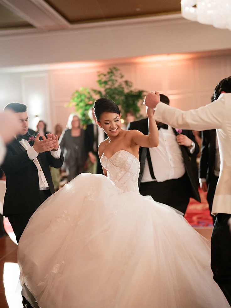 Groom lifting bride in a dip on the dance floor at their Turning Stone wedding in the Oneida Room, with a guest clapping beside them