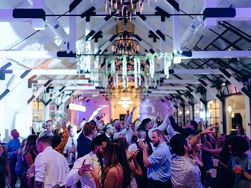 Wide view of a Greek Peak wedding reception inside The Lookout, with guests dancing beneath white-painted trusses, hanging greenery and tiered chandeliers