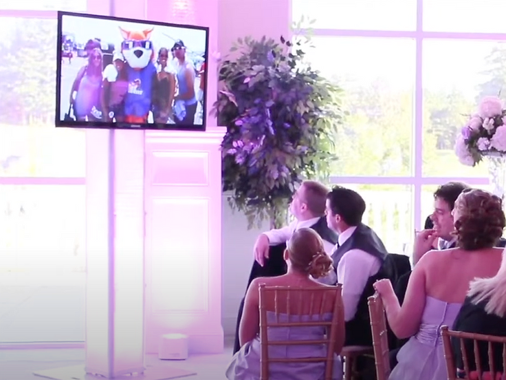 Flat-screen display on a pedestal showing a photo collage during a reception