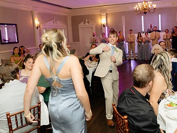 Wedding party members walking into a purple-lit reception hall as guests clap from their tables during the traditional grand entrance