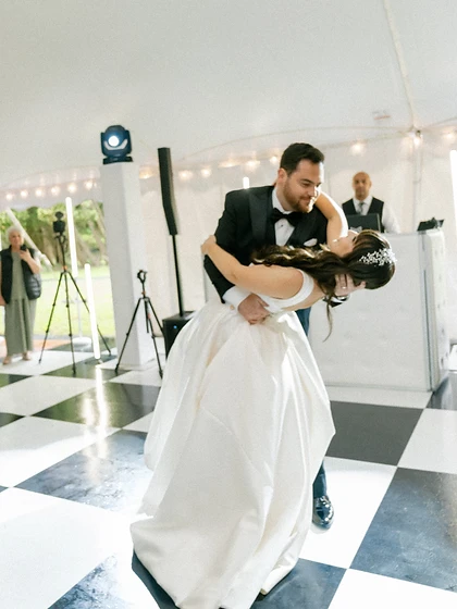 Newlywed couple in a dramatic dip on a black-and-white checkered dance floor inside an event tent