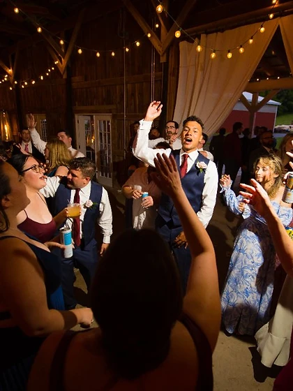 Guests dancing with arms raised on the dance floor of a rustic barn wedding reception