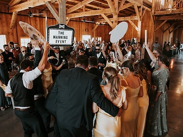 Wedding party cheering on the dance floor while holding a custom illuminated marquee sign and oversized props during a bottle service style entrance