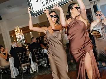 Bridesmaids in matching satin dresses carrying a custom lit marquee sign into the reception during a bottle service grand entrance